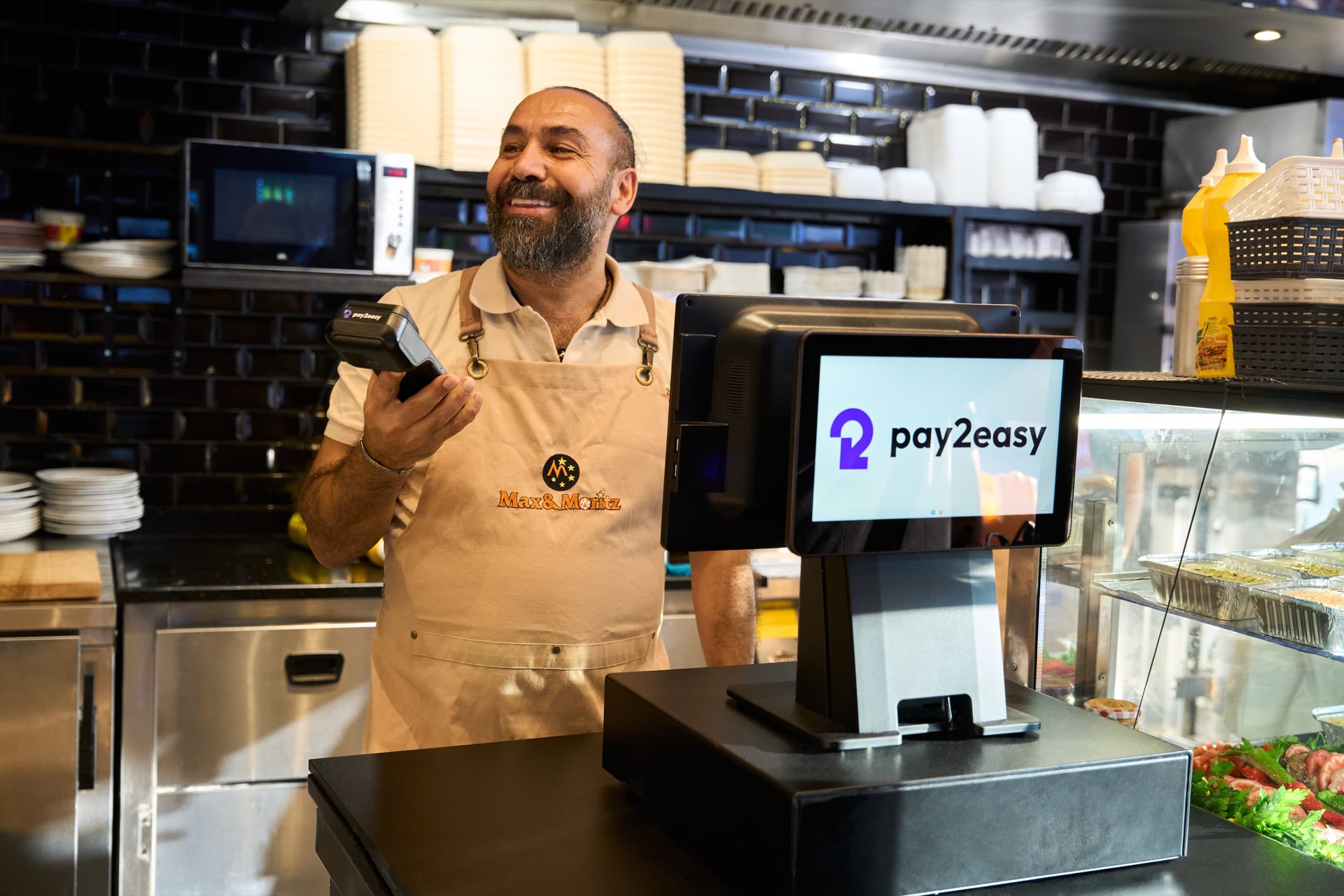 Barista handing a coffee to a customer beside a Pay2Easy POS terminal